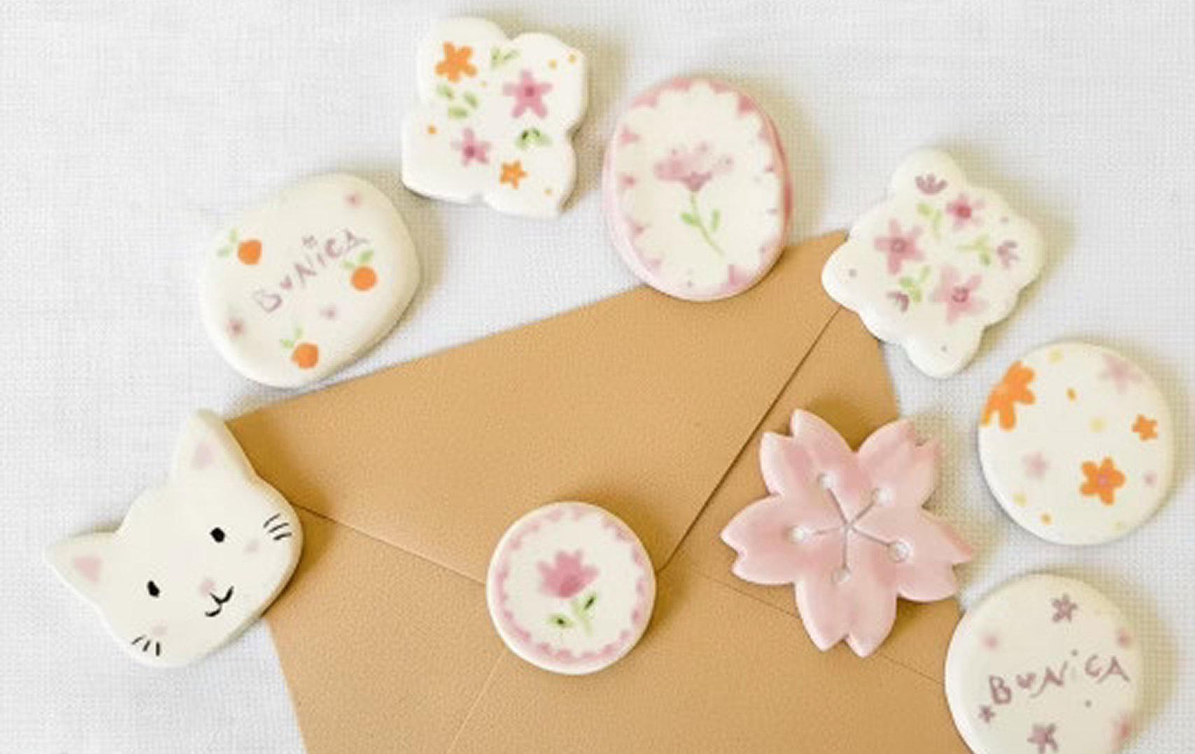 Imanes de ceramica, un gatito, y varios redondos con flores de colores pastel.